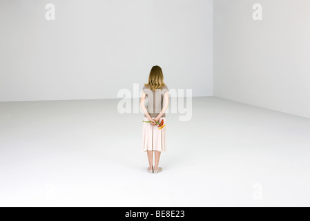 Woman standing alone, holding flowers behind back, rear view Stock Photo