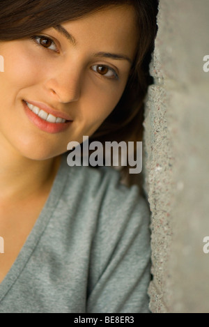 Young woman leaning against wall smiling, portrait