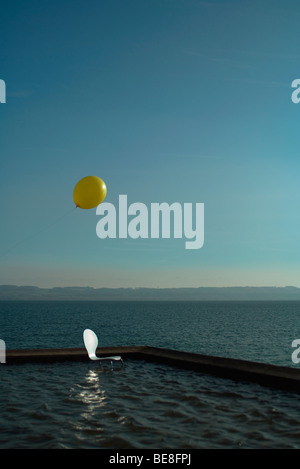 Chair placed in lake near breakwater, balloon floating overhead Stock Photo