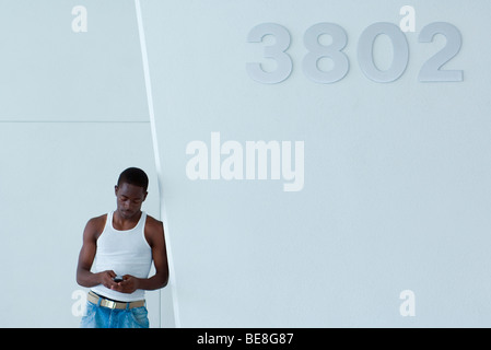 Young male leaning against wall, using cell phone to text message Stock Photo