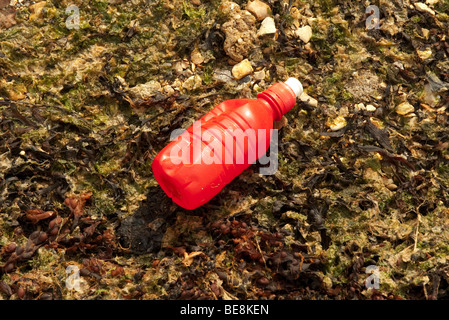 Red plastic bottle and rubbish washed up on beach Stock Photo
