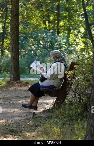 Elderly woman sits on the park bench and reads a religious book Stock Photo