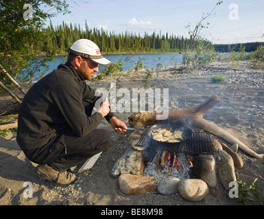 Man cooking, frying fish fillets in a pan on a camp fire, upper Liard River, Yukon Territory, Canada Stock Photo