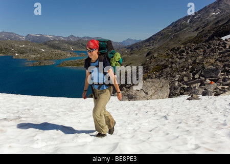 Young woman hiking, backpacking, hiker with backpack, snow field, descending towards summit of historic Chilkoot Trail, Chilkoo Stock Photo