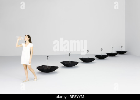 Woman drinking water from bottle, upside down umbrellas lined up behind her Stock Photo