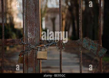 Padlocked or Locked rusty gates,with driveway and trees in background. An atmospheric shot, a little sinister, shot in Italy Stock Photo
