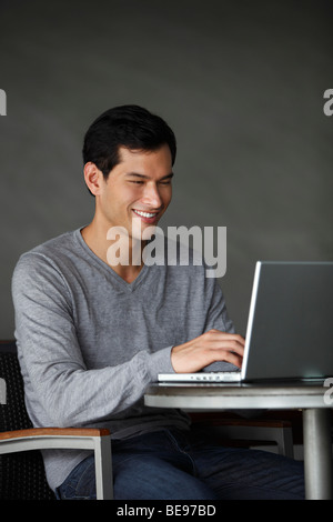 Asian man working on laptop, smiling Stock Photo