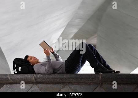 man lying down laying at back pack, reading a book Stock Photo