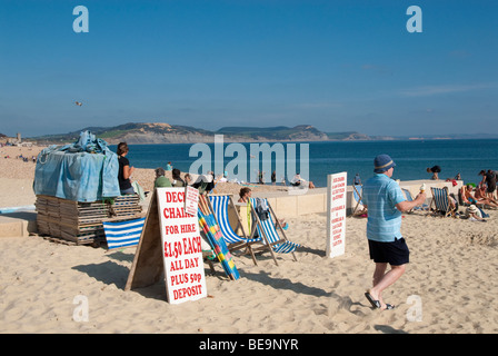 male holiday maker walking past deck chairs for hire on sandy beach Stock Photo