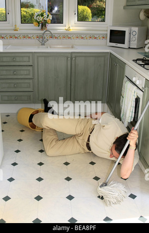 A man lying on a wet kitchen floor having tripped over the bucket Stock Photo
