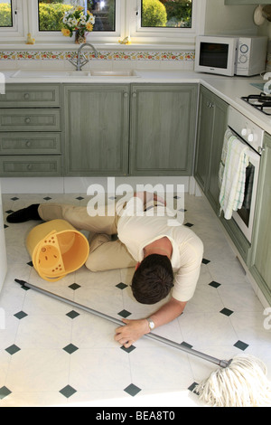 A man lying on a wet kitchen floor having tripped over the bucket Stock Photo