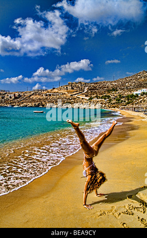 Beautiful island of Mykonos Greece with private beach called Super Paradise Beach and young shapely woman doing cartwheel Stock Photo