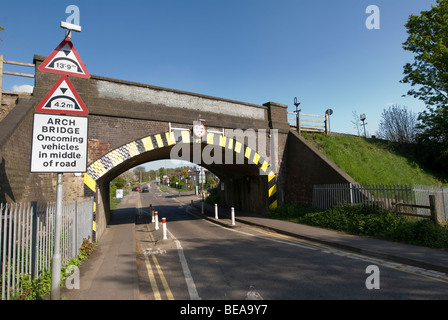 Road markings guiding traffic single file beneath a height restricted railway bridge in England Stock Photo