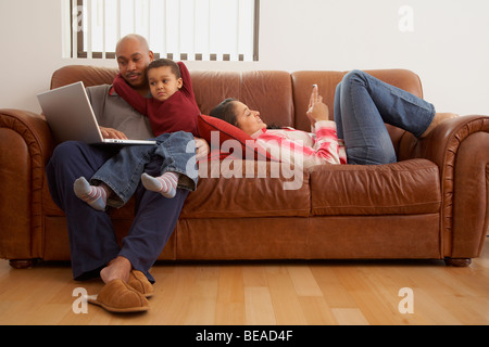 Antiguan man using laptop in living room with family Stock Photo