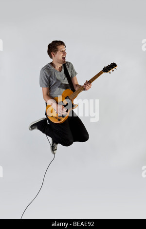 A musician playing a guitar and jumping in mid-air Stock Photo