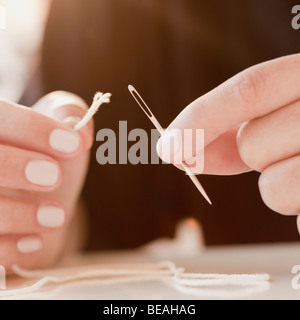 Woman stringing frayed thread through needle Stock Photo