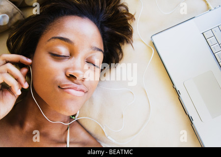 African woman listening to music on headphones connected to laptop Stock Photo