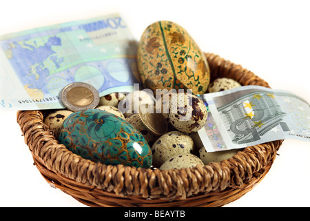 A basket full of quails and artificial eggs together with euro currency notes and coins. A financial or business concept Stock Photo