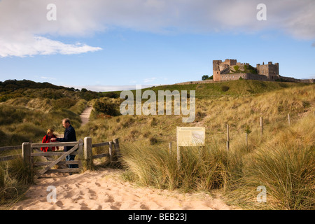 Bamburgh, Northumberland, England, UK. People on a path through sand dunes SSSI sign with Bamburgh Castle beyond Stock Photo