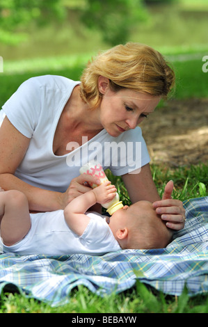 Mother helping baby drink milk from bottle outdoors Stock Photo