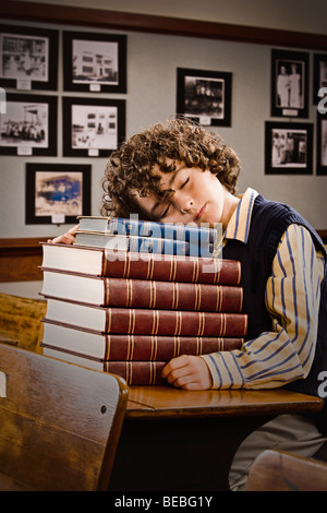 Schoolboy sleeping on a stack of books in a classroom Stock Photo