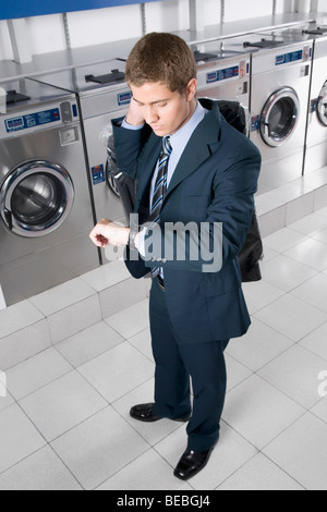 Businessman looking at wristwatch in a laundromat Stock Photo