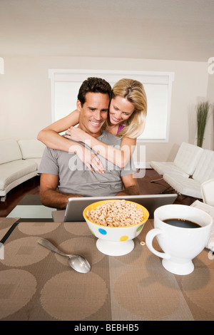 Man working on a laptop and a woman hugging him from behind Stock Photo