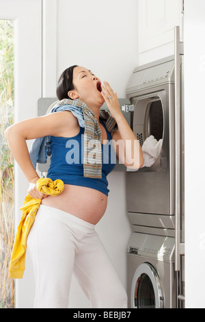 Pregnant woman yawning in front of a washing machine Stock Photo