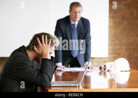 Businessman leaning on a table with blueprints. Young executive using laptop computer covering face in boardroom Stock Photo