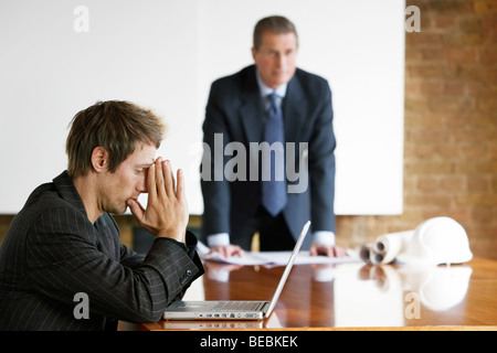 Businessman leaning on a boardroom table with blueprints. Young executive using laptop computer Stock Photo