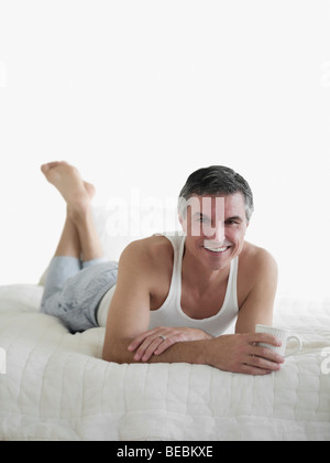Man lying on the bed holding a cup of coffee and smiling Stock Photo