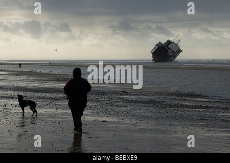 A dog walker passes the ferry Riverdance, beached at Cleveleys, on the Fylde Coast in Lancashire. Stock Photo