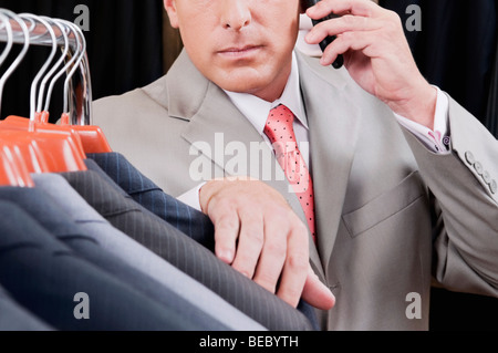 Businessman selecting a suit and talking on a mobile phone in a clothing store Stock Photo