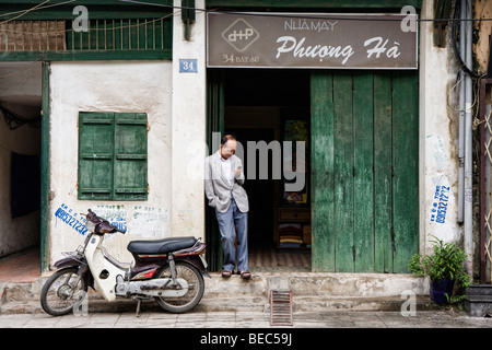 Man using a mobile phone standing outside a shop in Hanoi, Vietnam Stock Photo