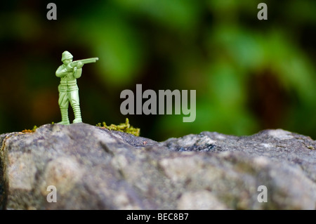A green plastic toy soldier takes aim with his rifle in the rugged outdoors. Stock Photo