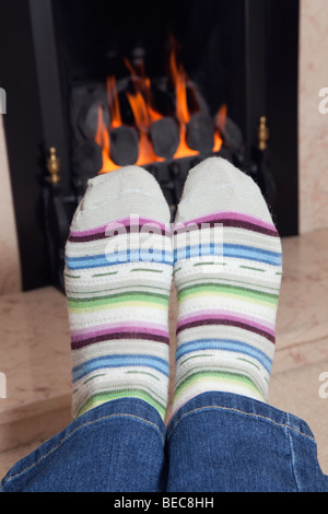 Close up of a pair of cold feet in cosy stripy wool socks warming in front of a coal gas fire in a fireplace at home in winter. UK Stock Photo