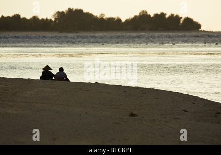 Two local women sitting on the beach in Gili Meno with the Island of Gili Trawangan on the foreground. Lombok, Indonesia Stock Photo