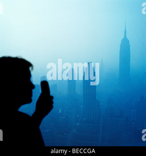 woman with cell phone looking at New York City skyline from sky scraper rooftop Stock Photo