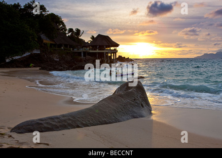 Typical granite rock of the Seychelles on the beach at dusk near Glacis, Sunset Beach Resort at back, island of Mahe, Seychelle Stock Photo