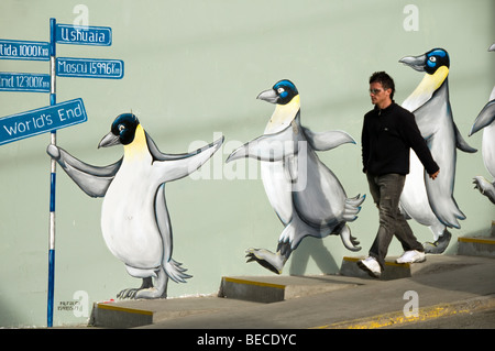 A man walking by a painting of a group of penguins on a wall in downtown Ushuaia, Argentina Stock Photo