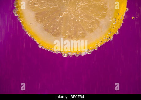 Close-up image of a section of lemon slice surrounded by bubbles of water Stock Photo