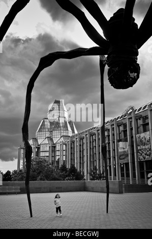 A yong girl stops to stare up at 'Maman'; a giant spider sculpture created by Louise Bourgeois dwarfs the National Art Gallery. Stock Photo