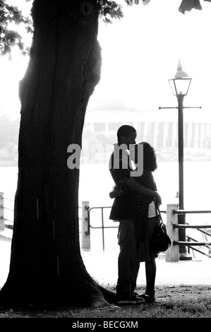 Silhouetted couple take shelter from rain under a tree while holding each other in a romantic embrace. Stock Photo