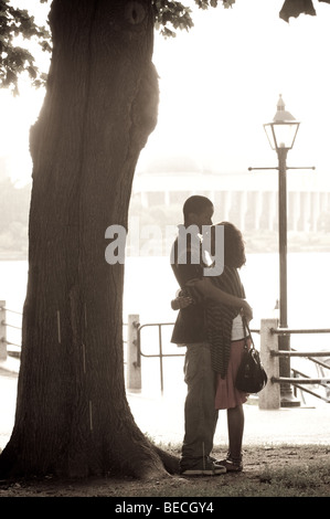 Silhouetted couple take shelter from rain under a tree while holding each other in a romantic embrace. Stock Photo