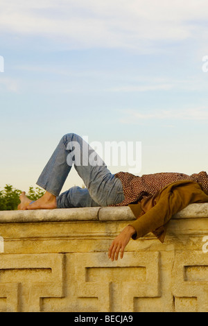 Side profile of a young man lying on a stone wall Stock Photo