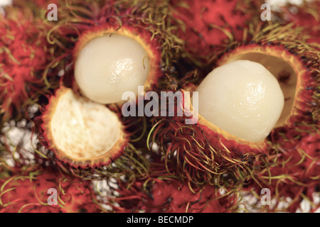 A pile of rambutan fruits with two opened to reveal the delicious interior Stock Photo