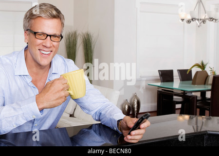 Man drinking coffee and text messaging on a mobile phone Stock Photo