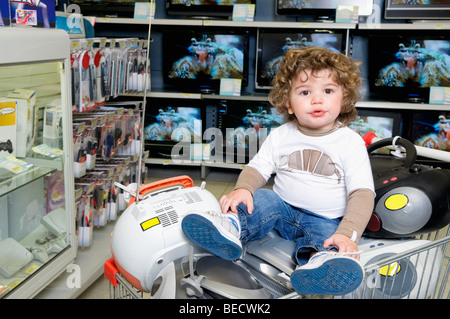 Baby boy sitting on a shopping cart in a supermarket Stock Photo