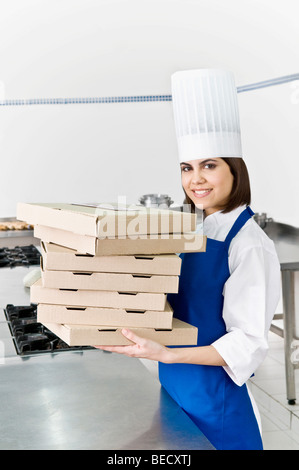 Female chef holding stack of pizza boxes and smiling Stock Photo