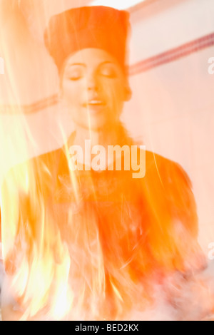 Female chef behind the flame in the kitchen Stock Photo